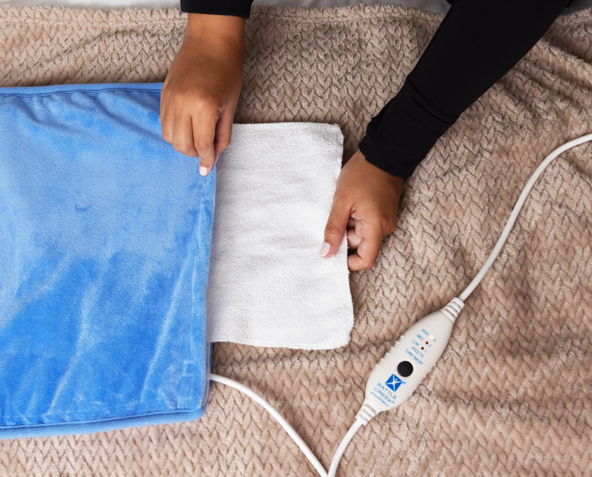 Person using an electric heating pad on a bed