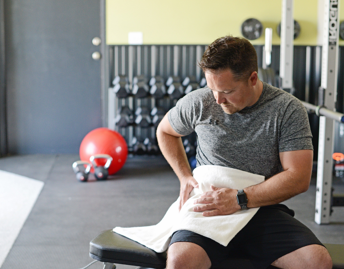 man using thermophore heating pad on hip in gym setting